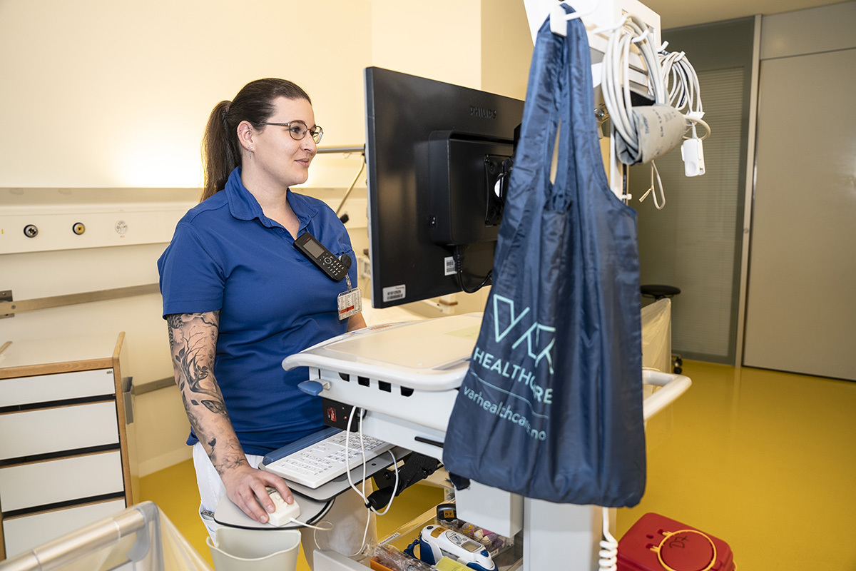 Eine Pflegefachfrau steht im Patientenzimmer am PC.